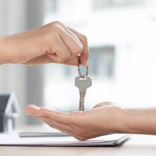 Twee handen waarvan een huissleutel aan de ander geeft 